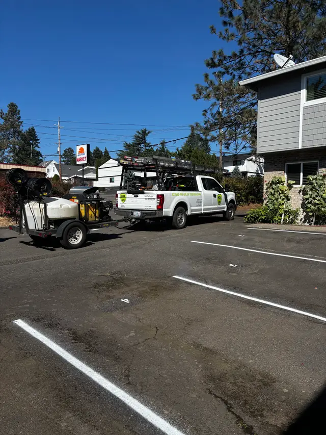 HOA Services pickup towing a pressure-washing trailer beside freshly striped parking spaces